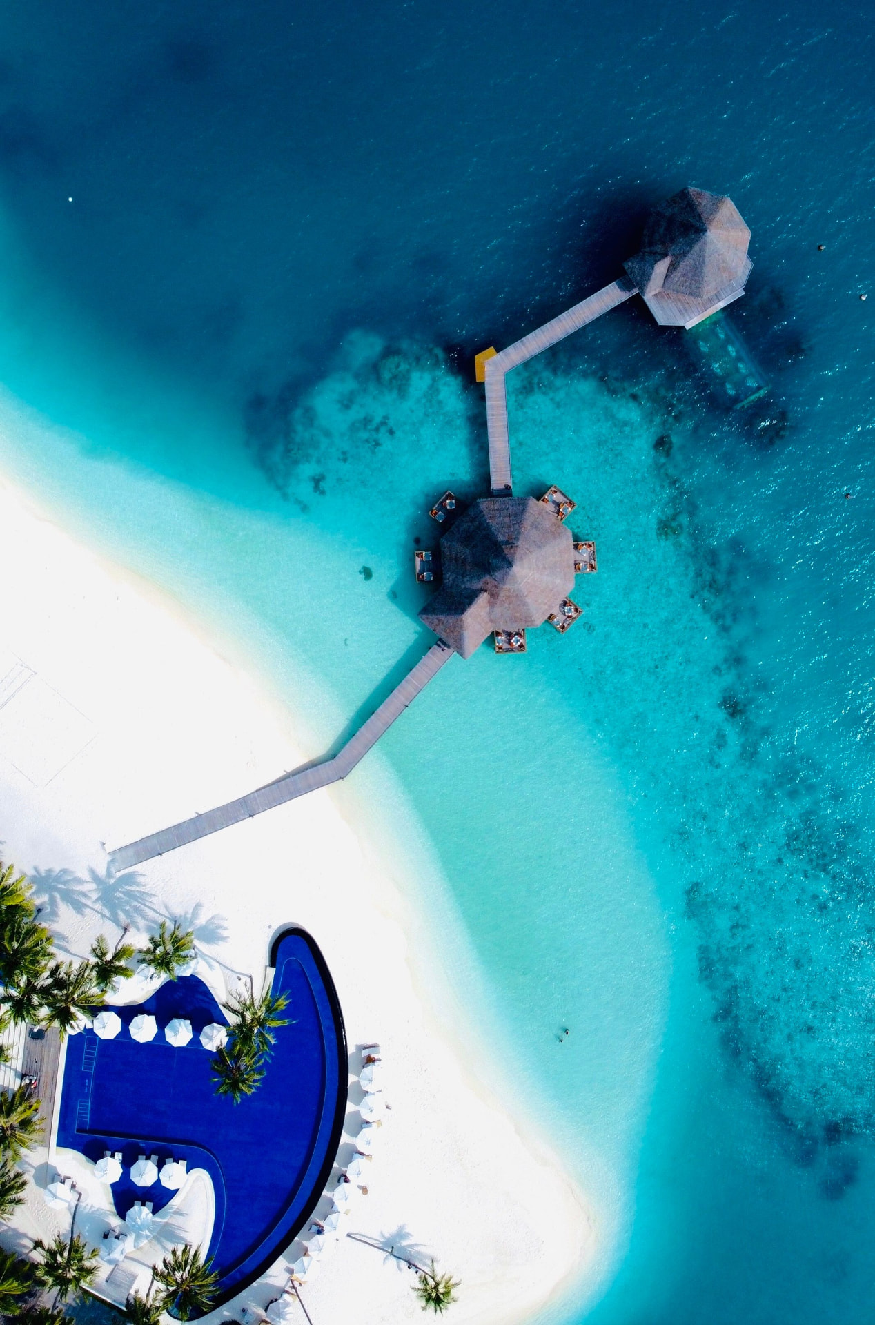 Vista aérea de playa de arena blanca, embarcadero y piscina junto a la laguna turquesa en las Maldivas